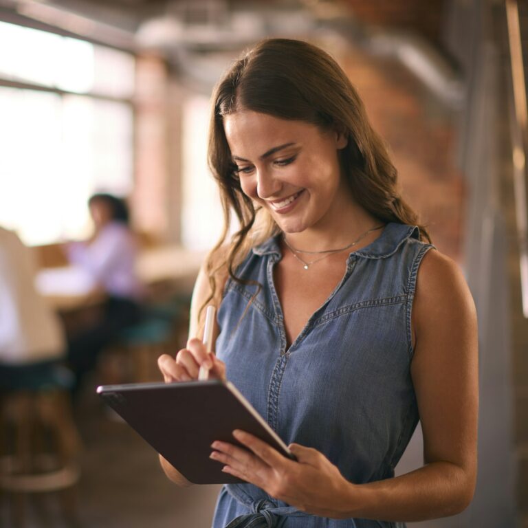 Businesswoman Using Digital Tablet And Stylus Pen Working In Office With Colleagues In Background