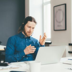 Concentrated young man operator in headset and casual wear talking with client on laptop in office