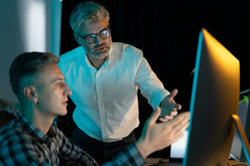 Senior Mentor Guiding Employee In Office During Evening Work Session