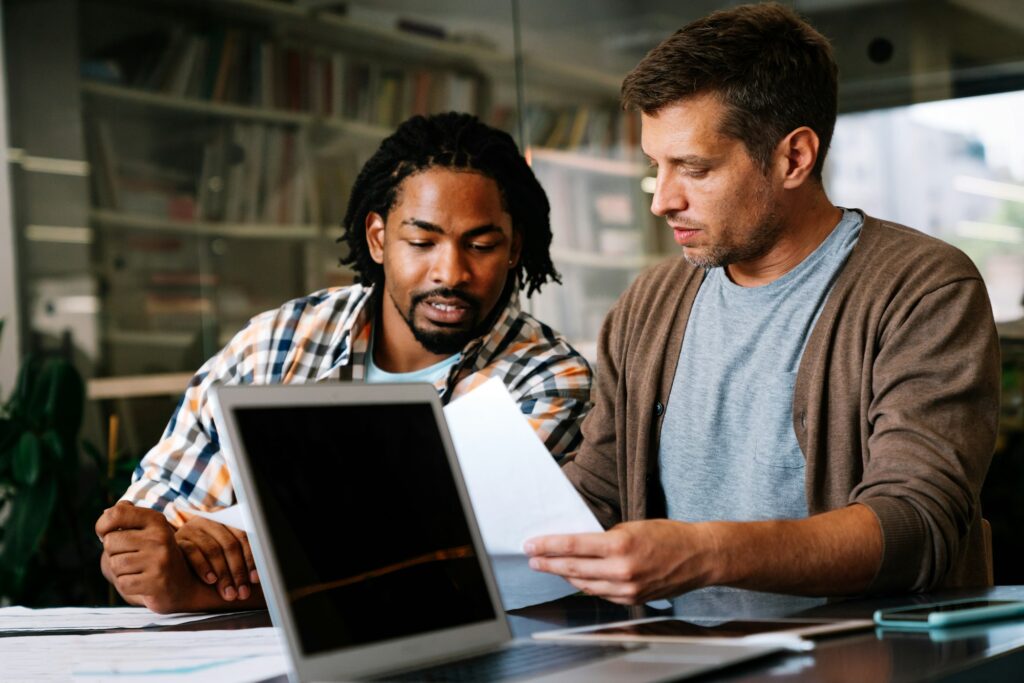 Young manager talking with experienced colleague while using computer in office.